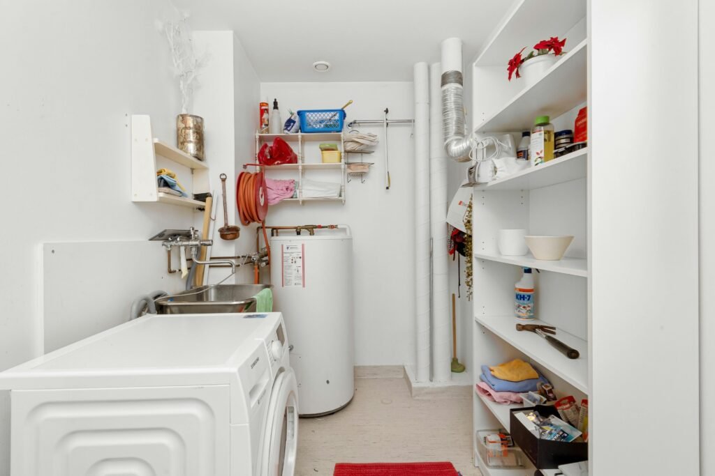 pexels-photo-19980200-19980200 Clean and organized home laundry room with washing machine, shelves, and water heater.