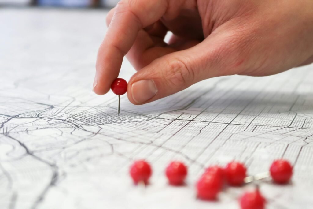 pexels-photo-7663519-7663519 Close-up of a hand placing a red pin on a map indicating geographic location pinning.